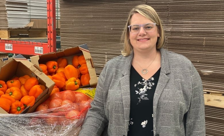 Smiling woman in glasses posing in front of a crate filled with onions and red peppers