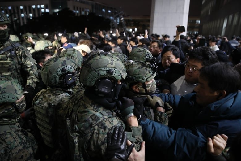 Dozens of troops are seen shoulder to shoulder, with several Asian men seen trying to get past them in a nighttime scene.