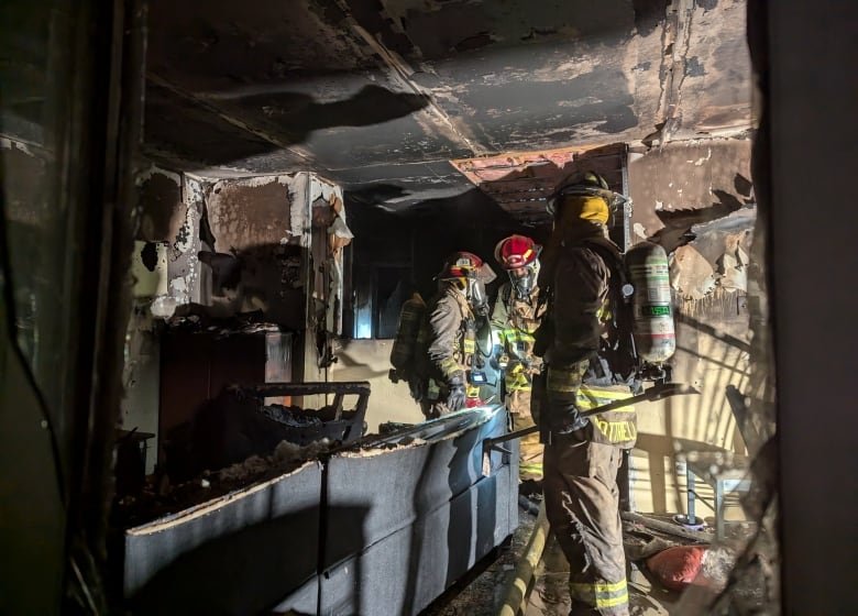 Three firefighters inside a dark, burnt home.