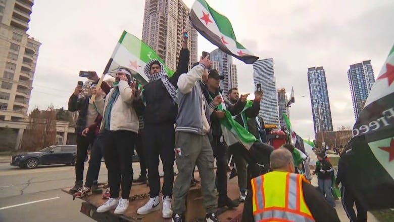 People waving a Syrian flag stand on a wooden float while cheering. 