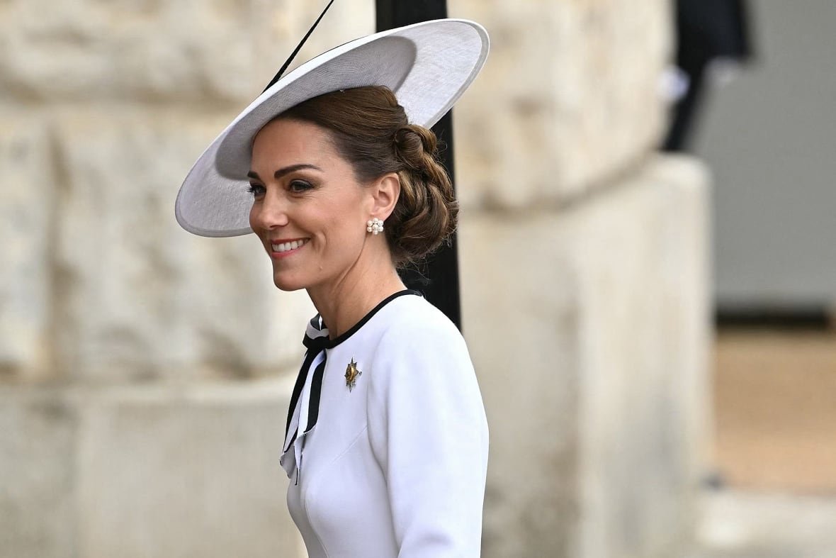 A person wearing a fancy hat smiles while walking.