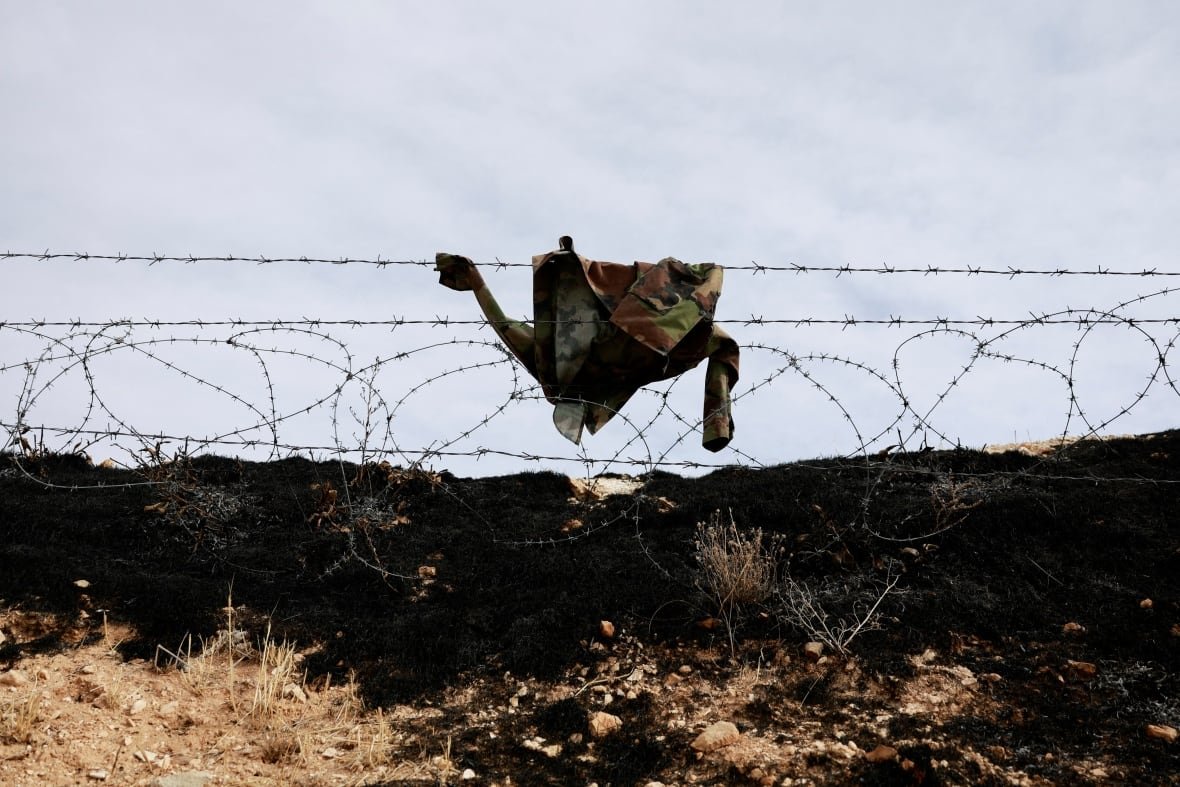 A uniform of a soldier hangs on barbed wire.
