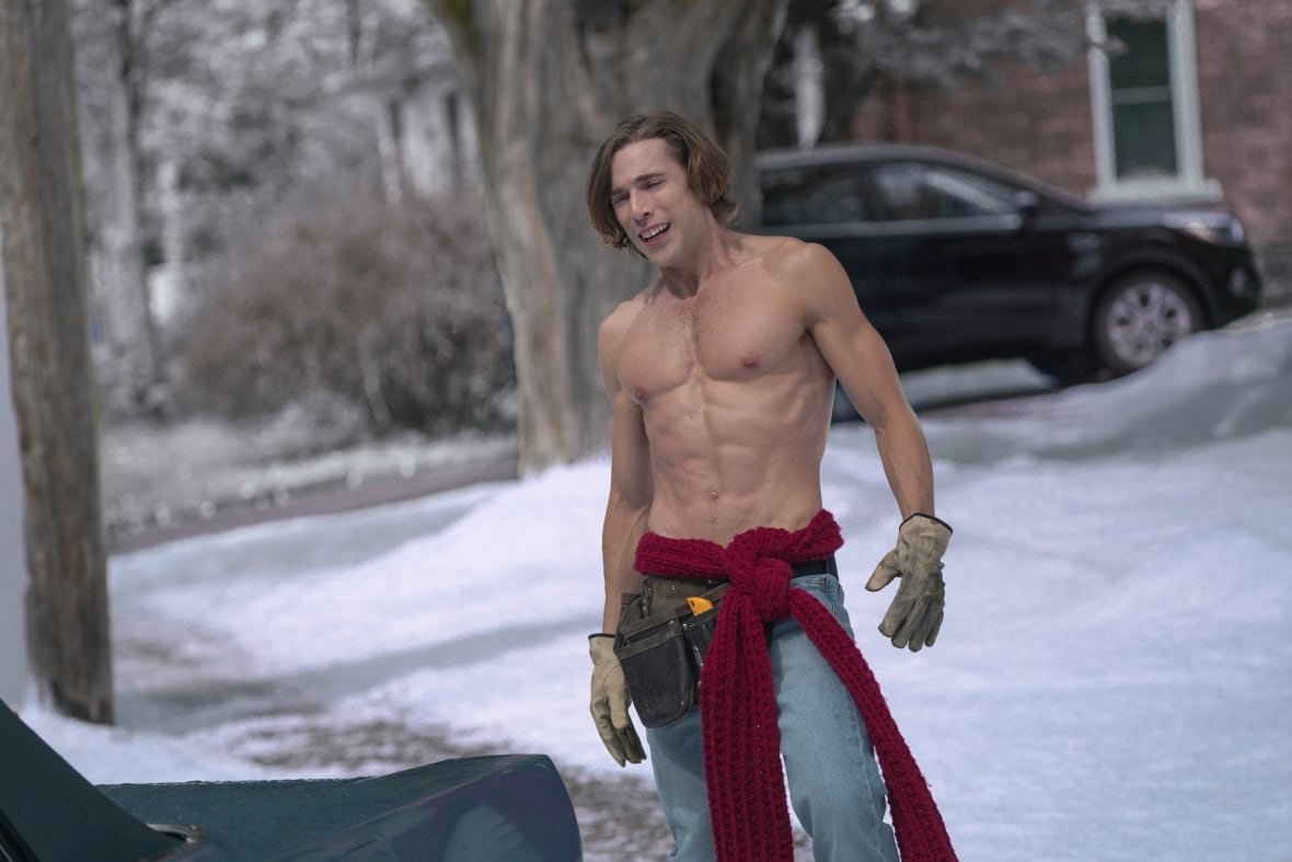 A muscular, shirtless man poses while standing in the snow.