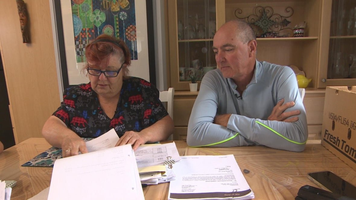 A woman with short hair and glasses sits beside a man who is balding as they look over documents. 