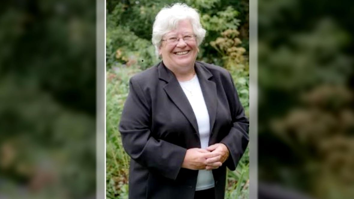A photo of a short lady wearing a dress suit with grey hair and glasses.