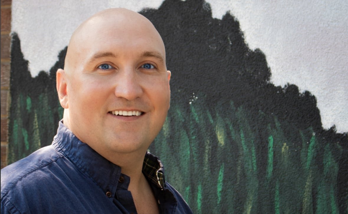 A portrait of a bald man wearing a blue shirt. 