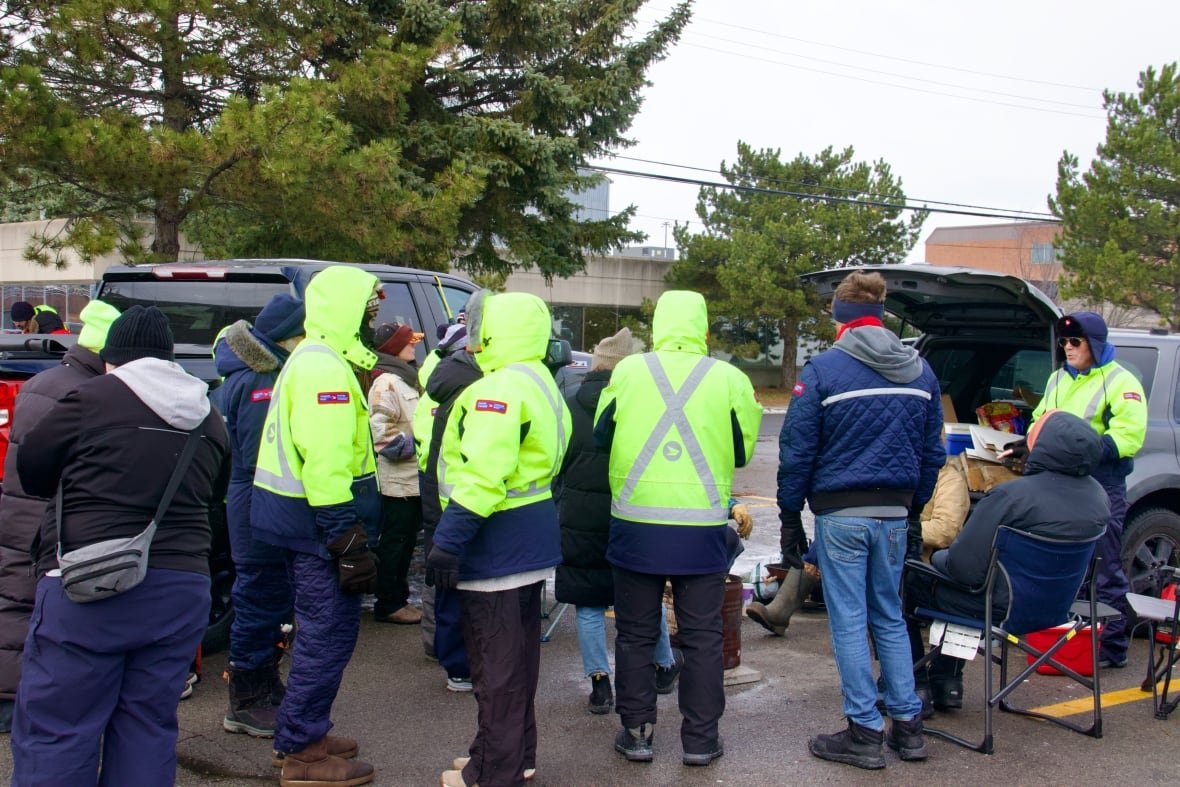 A group in green high-vis coats and winter jackets huddle between a group of trucks.