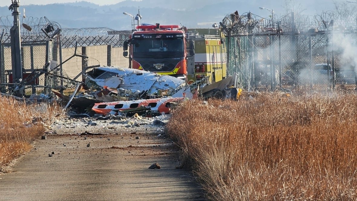Smoldering wreckage of a downed plane is seen in a field as a firetruck is seen parked behind it.
