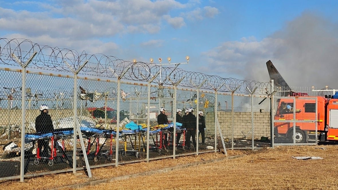 Emergency workers wearing transport stretchers behind a barbed wire fence.