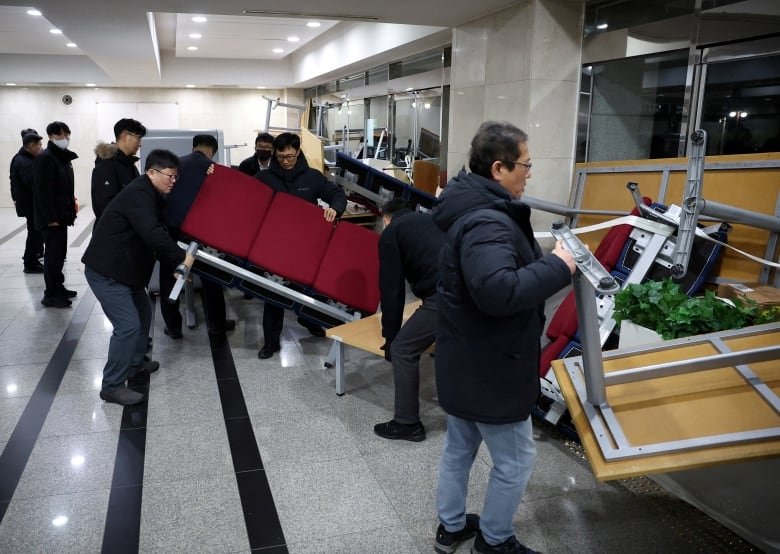 People remove furniture that has been piled up to form a barrier blocking doors.