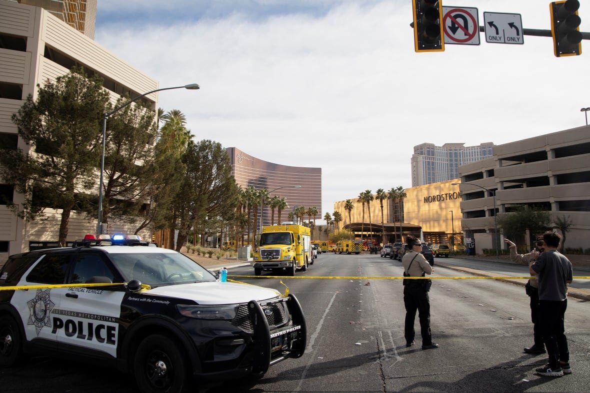Law enforcement officers stand behind yellow tape in a cordoned area.