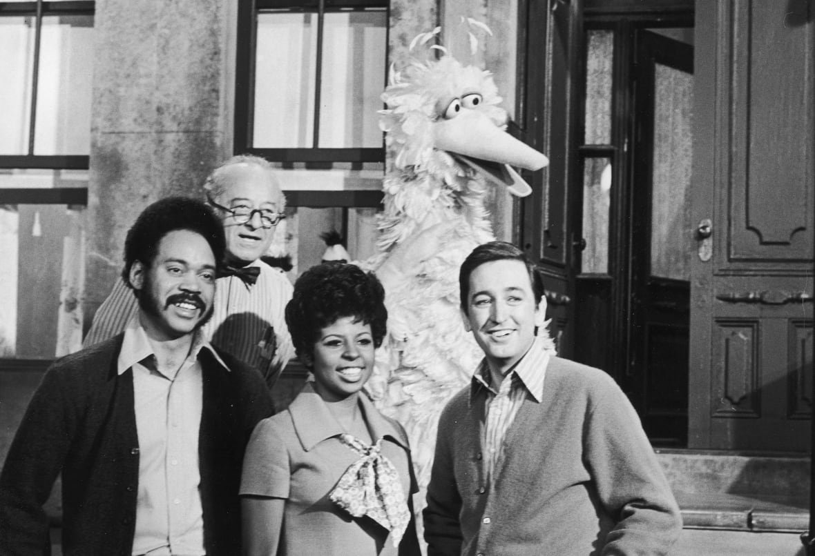 A black and white photo of four adults and a muppet