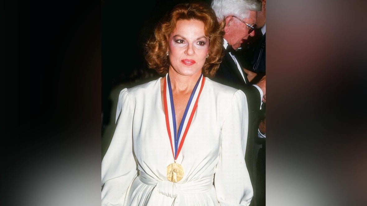 A woman is pictured in a white dress, with a medal around her neck. 