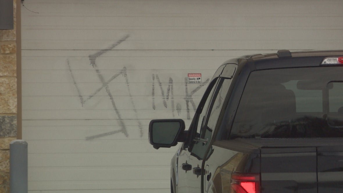 The graffiti of a swastika is sprayed painted in the parking lot door of a condo building.