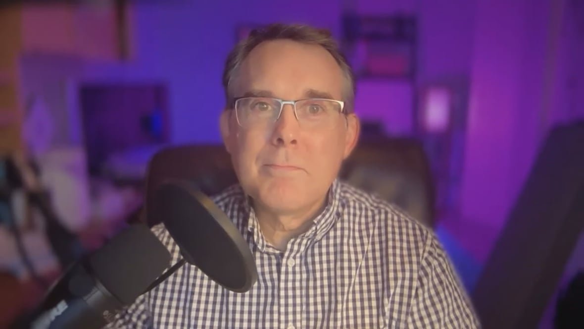 A man sits in front of a podcast microphone, with purple lighting behind him.