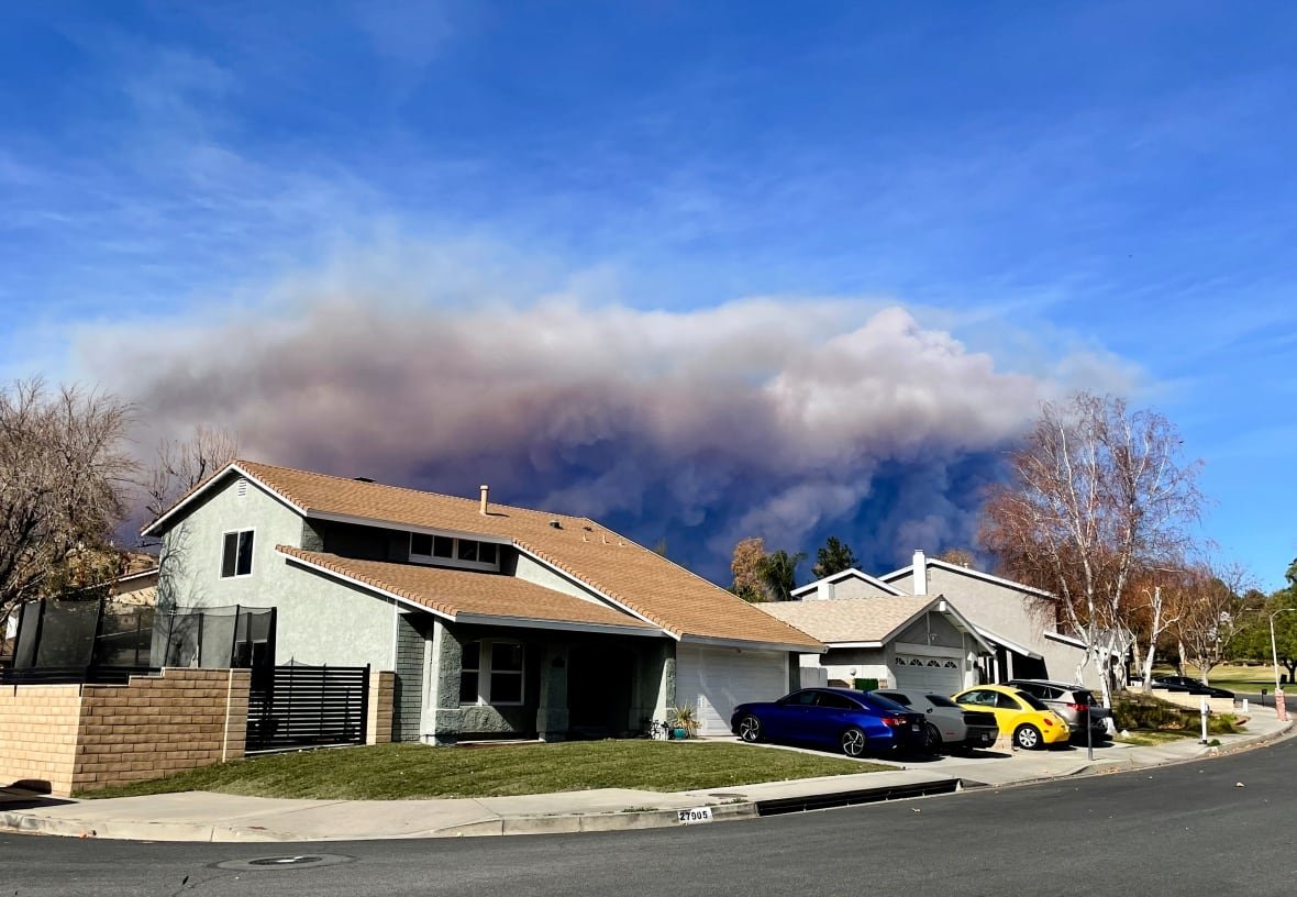 A large plume of smoke rises behind a house.