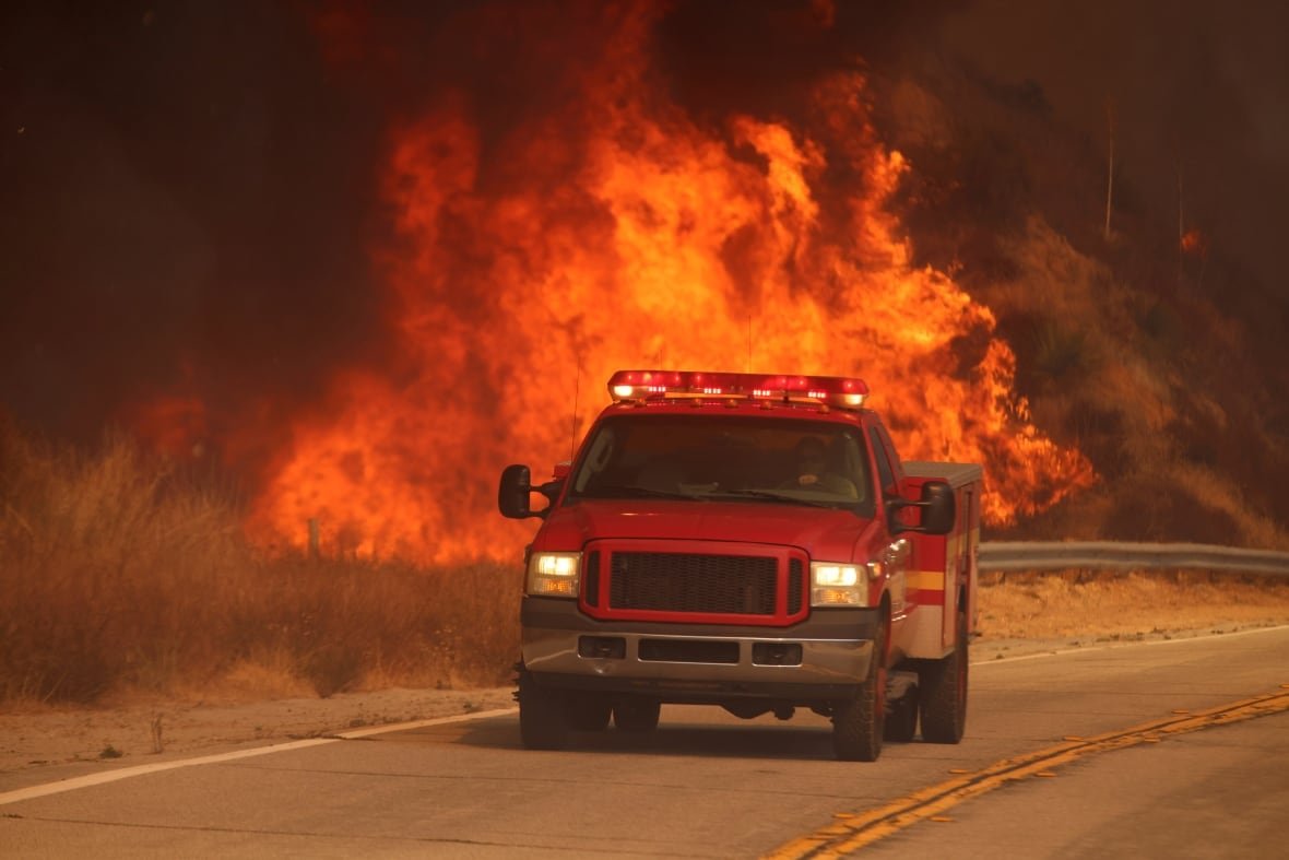 A firetruck drives past flames.