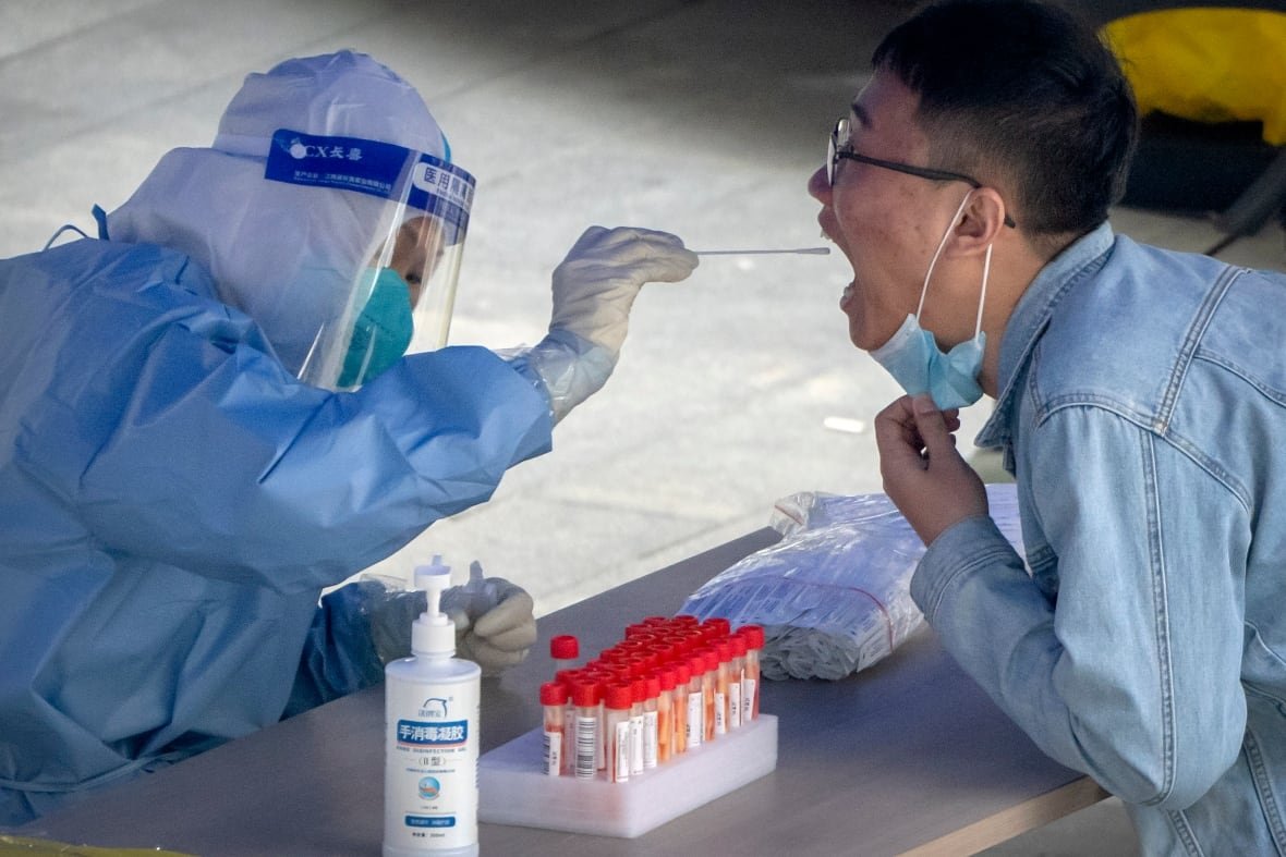 Person in protective suit holds a swab near a man's open mouth.