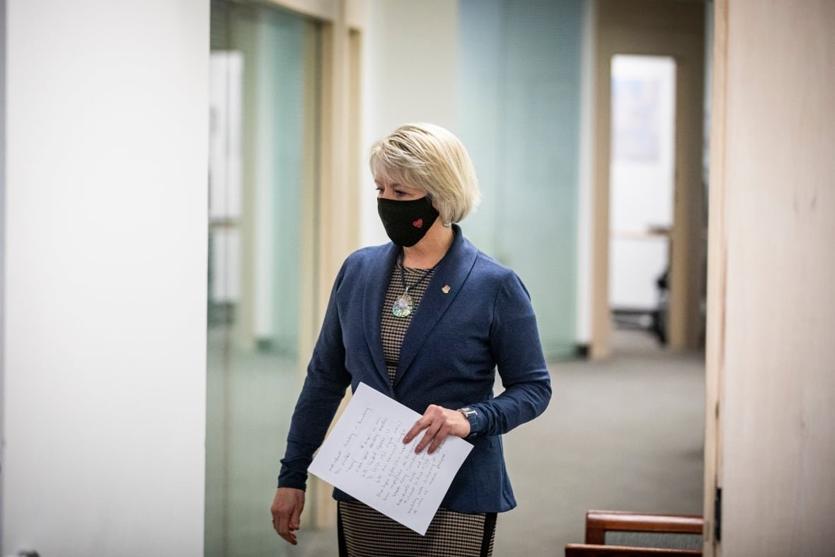 A blonde woman wears a mask and holds a piece of paper.