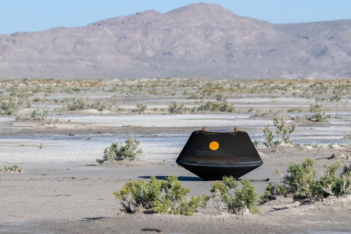 Black capsule in the desert with mountains in background