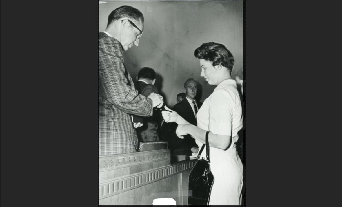 A woman signs an autograph for a man in a courtroom.
