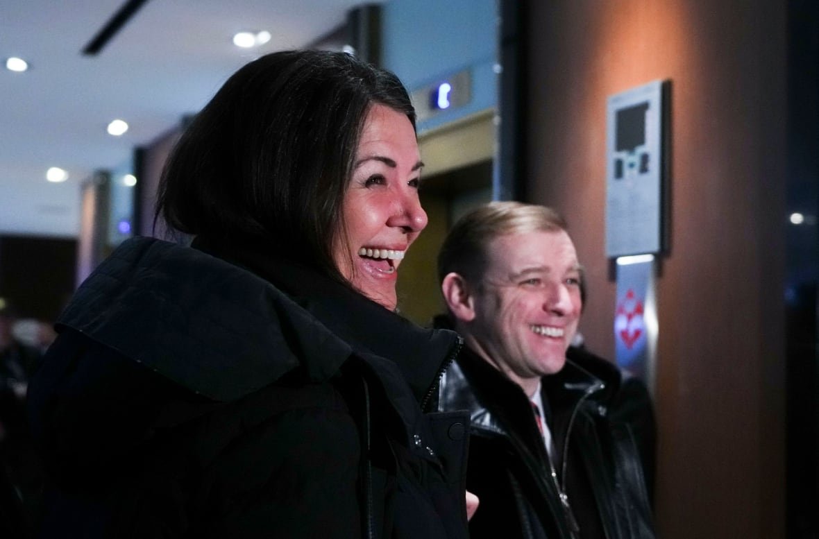 A man and a woman in winter coats smile for a photo.