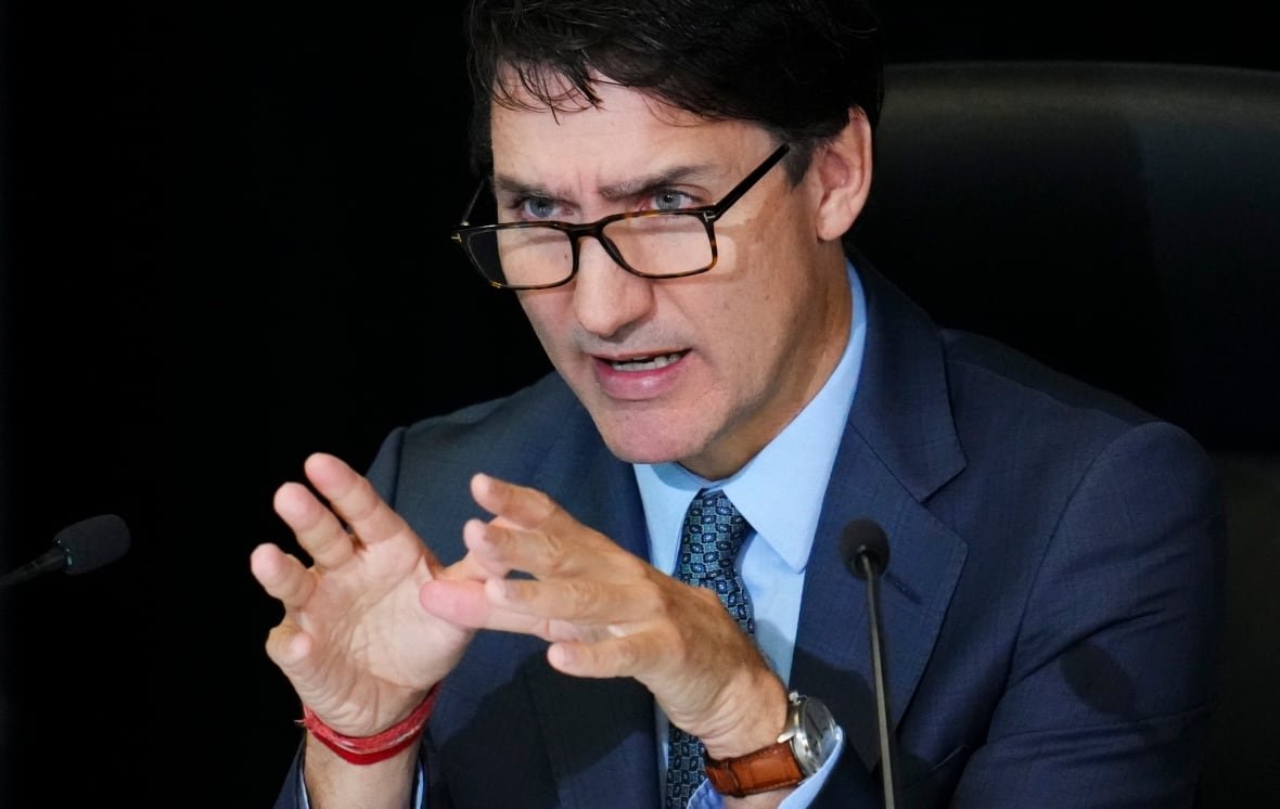 A man in glasses gestures with his hands as he speaks into a microphone.