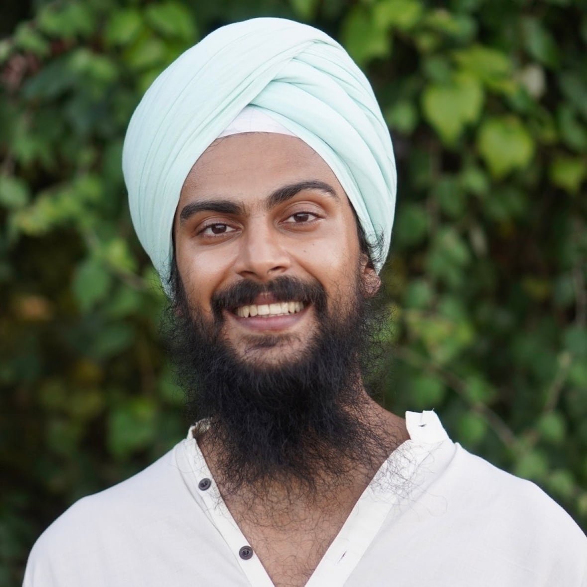 A man standing outdoors in a white shirt and blue turban. 