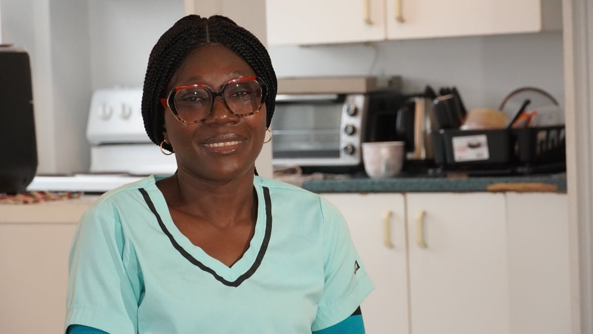 A woman in light blue scrubs is seated in front of a kitchen counter.