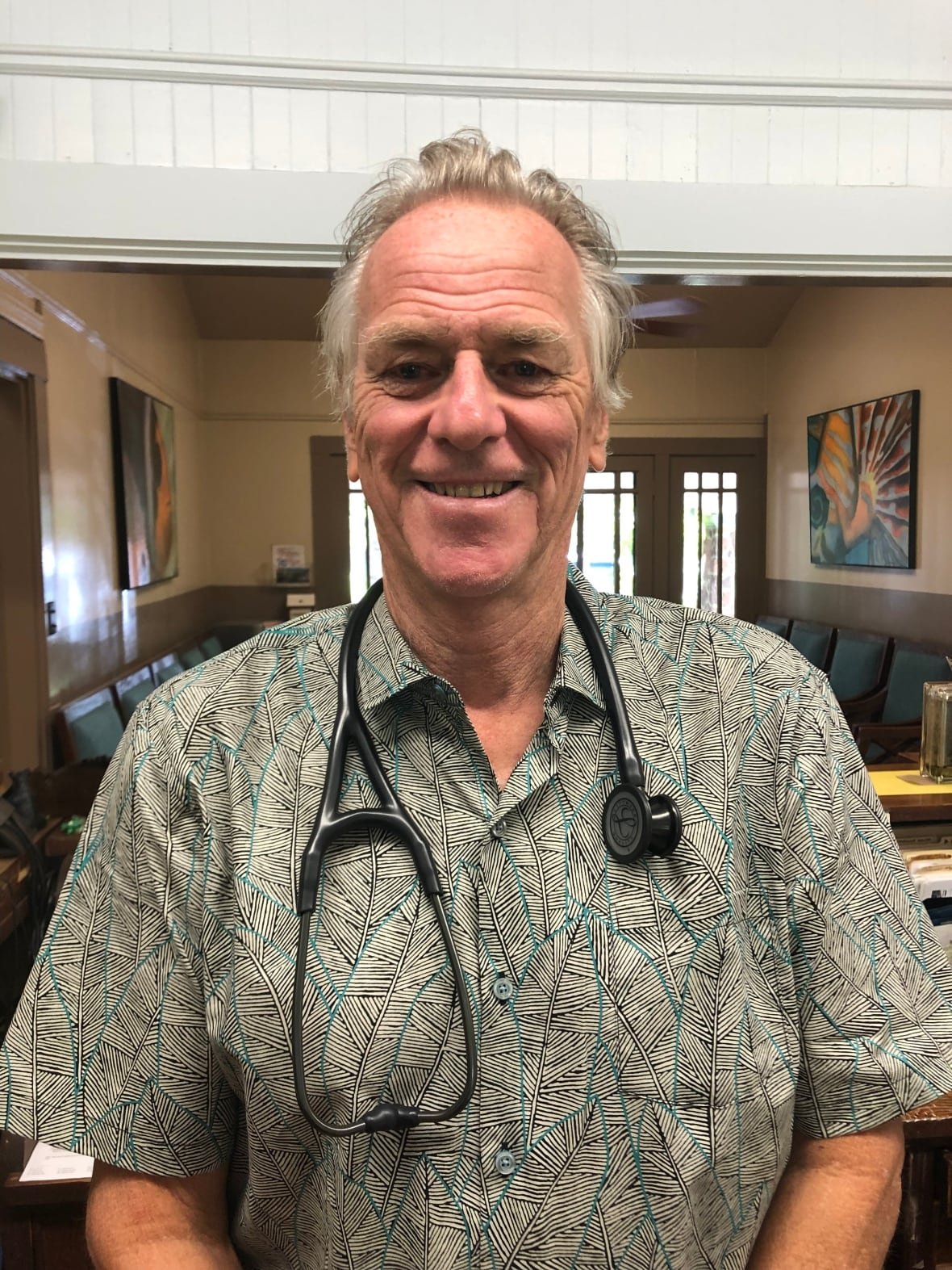 A portrait of Michael Murray in his Hawaii clinic, pictured with a stethoscope around his neck.