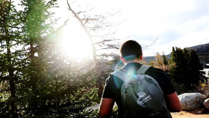 The sun shines on a teenage boy walking away. 