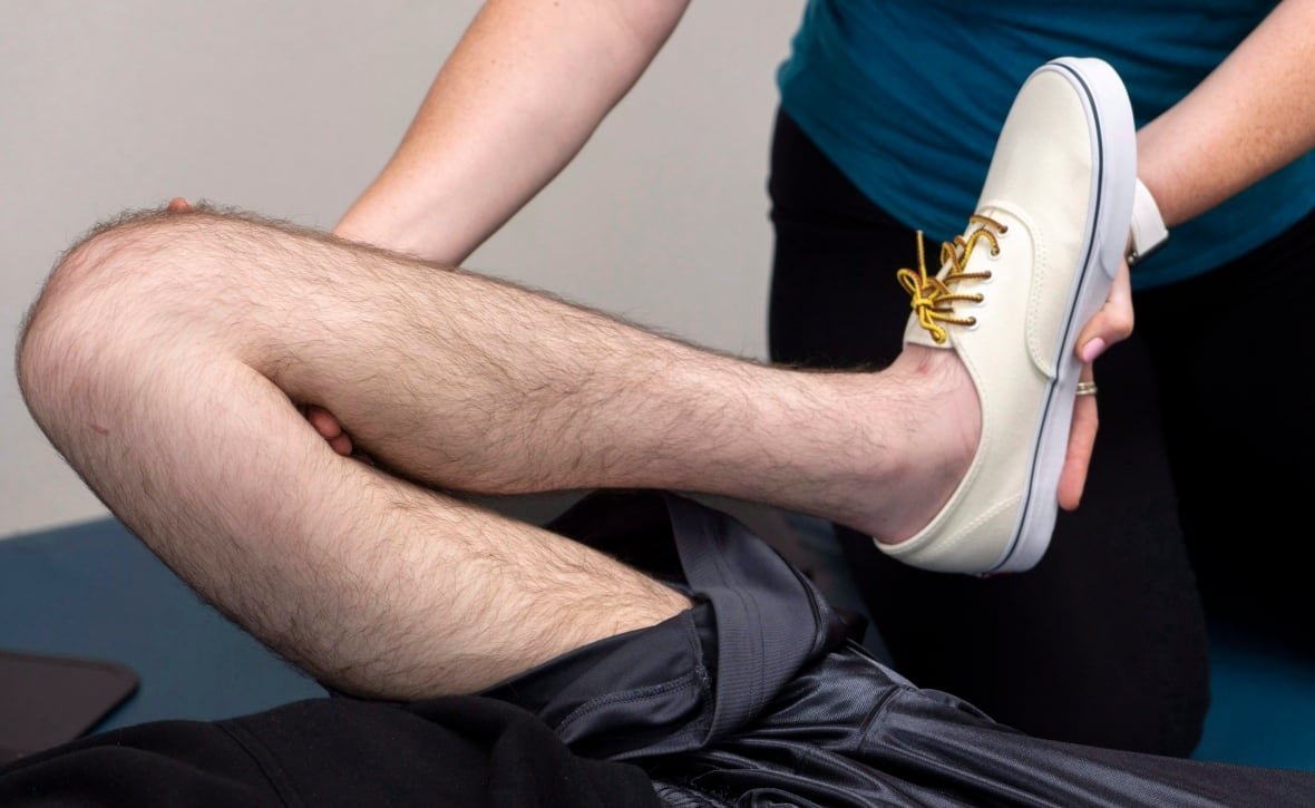 A man works on his legs during a physiotherapy session. His leg and the therapist's hands are visible. 