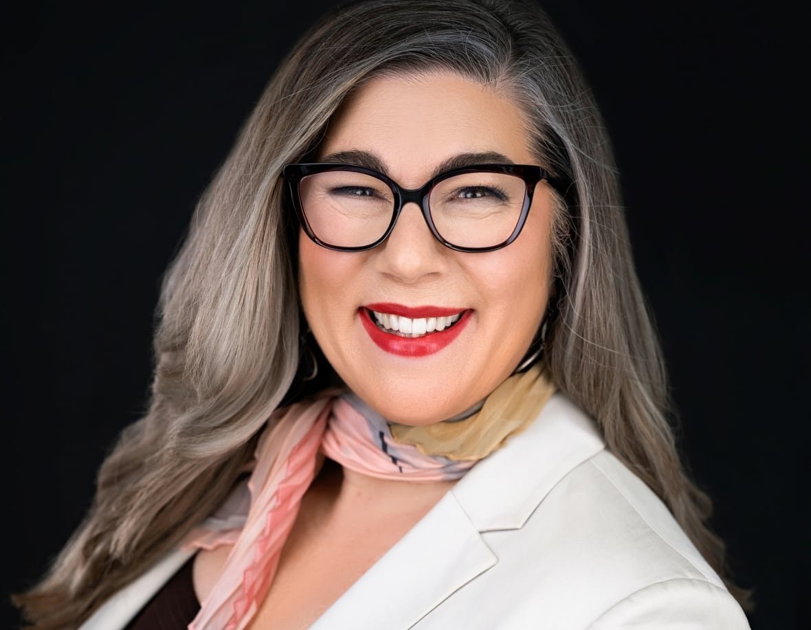 A portrait of a smiling woman in white blazer and a pink patterned neck scarf.
