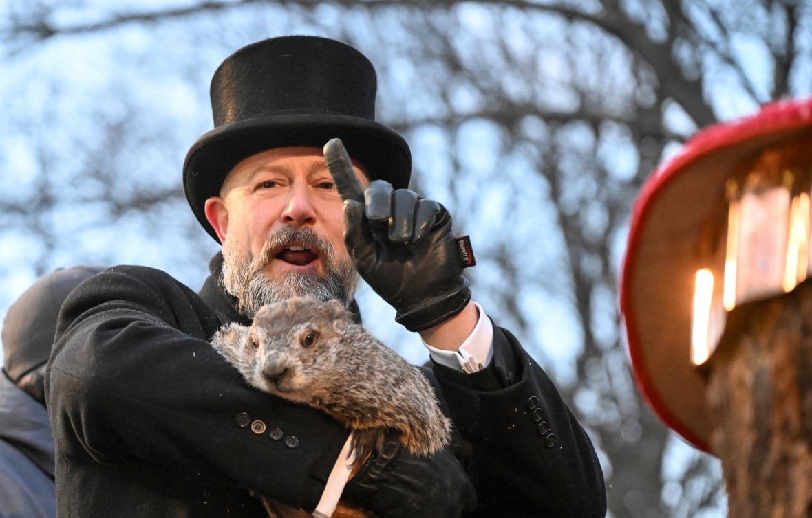 A man in a tophat holds a groundhod.
