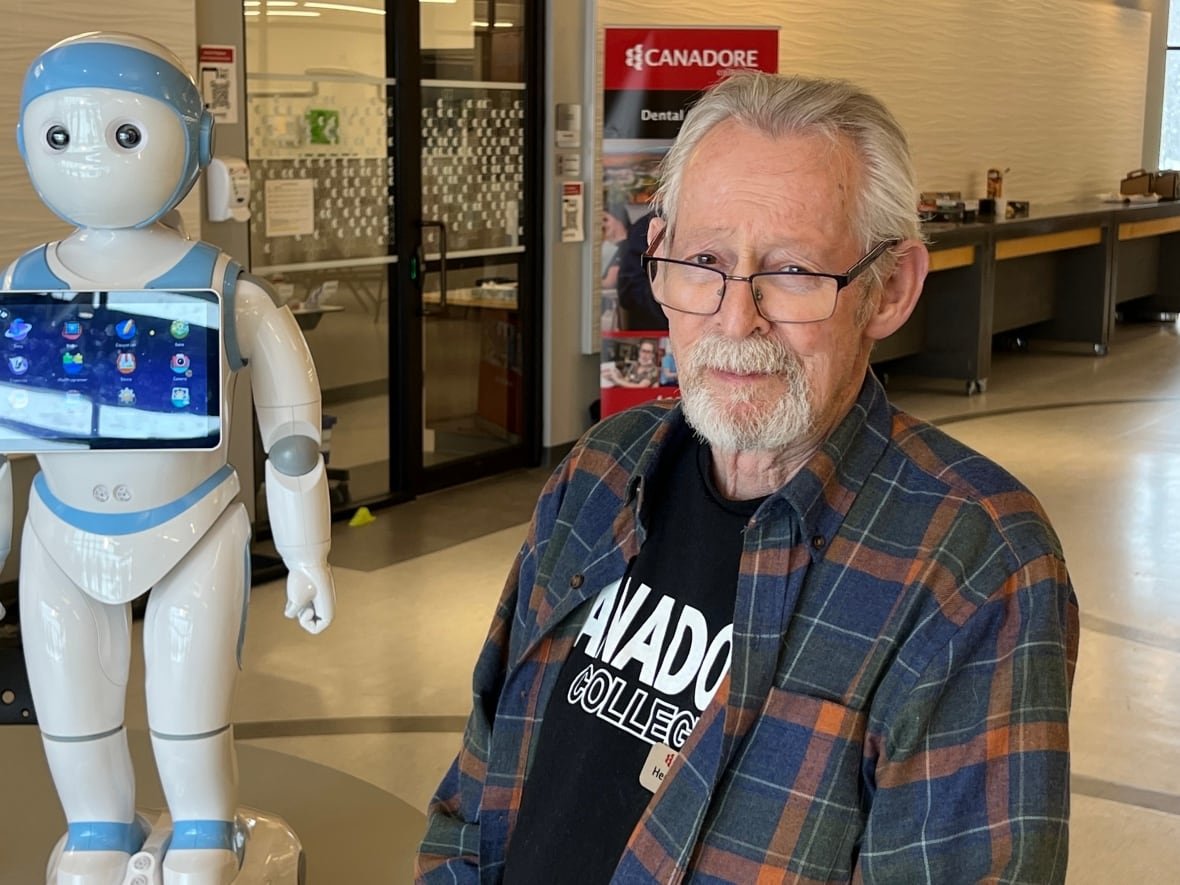 An older man poses next to a white and blue robot. 