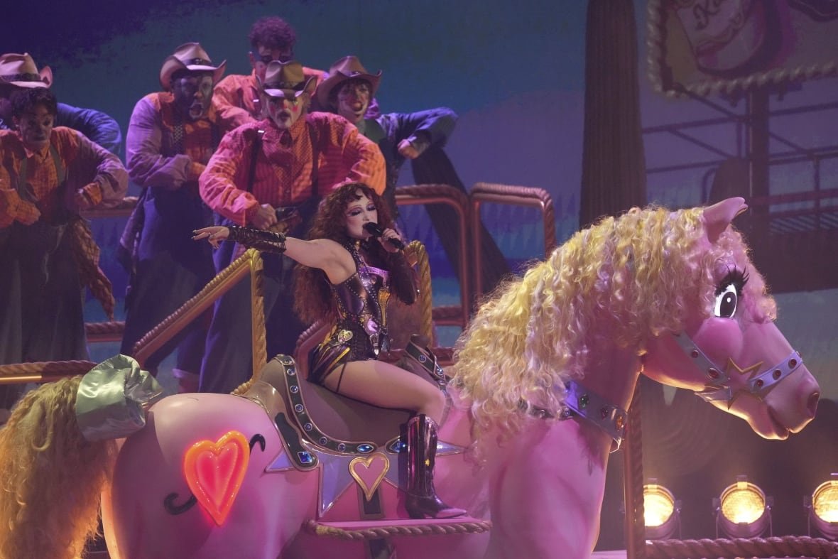 A woman sits on a giant pink horse, performing a song. 