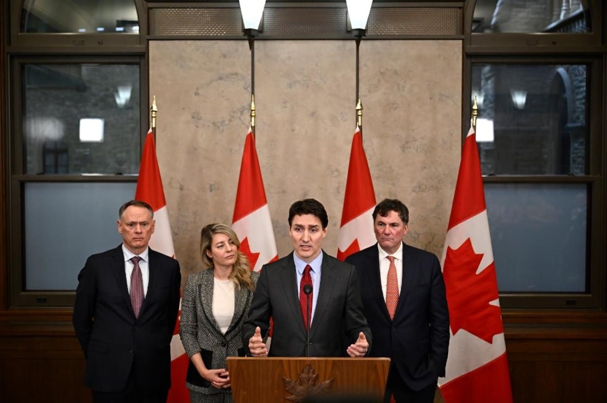 Four people stand at a podium in front of Canadian flags.