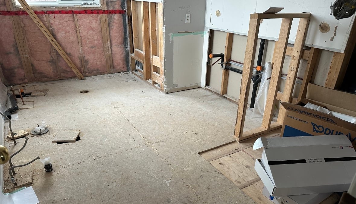 A mostly vacant room littered with debris and and missing drywall. 