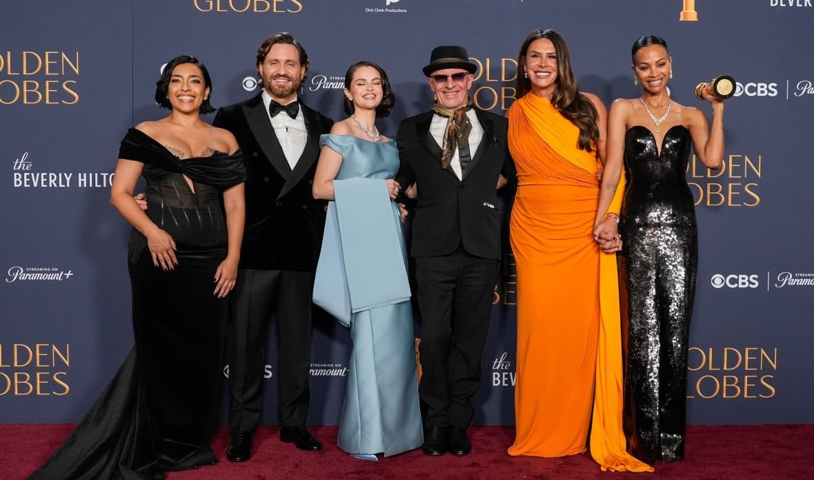 Six people pose for a photo in front of a blue backdrop that says "Golden Globes" on it. They are all wearing fancy outfits, and the woman on the far end is holding an award.