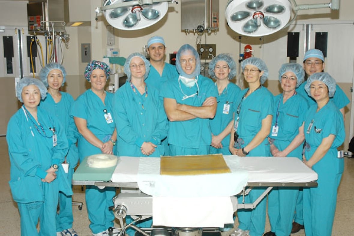 The neurosurgery team at UBC stands in front of a table, wearing blue scrubs, with Dr. Christopher Honey standing in the middle.