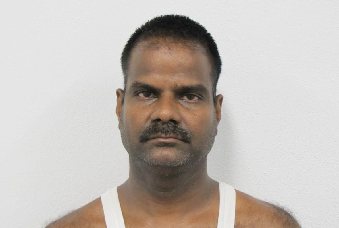 Mugshot photo of a man with a mustache and wearing a tanktop.