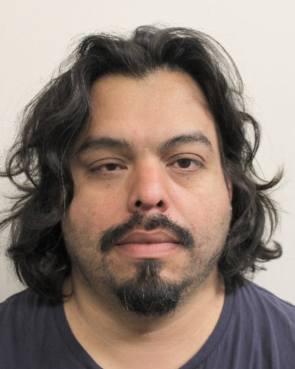 The photograph is of a man with a goatee and unkempt black hair.