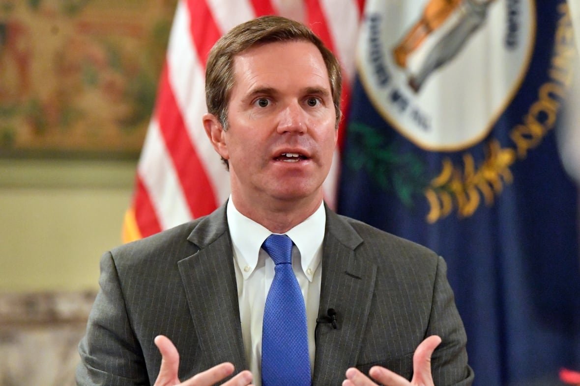 Andy Beshear speaks while wearing a grey suit and blue tie