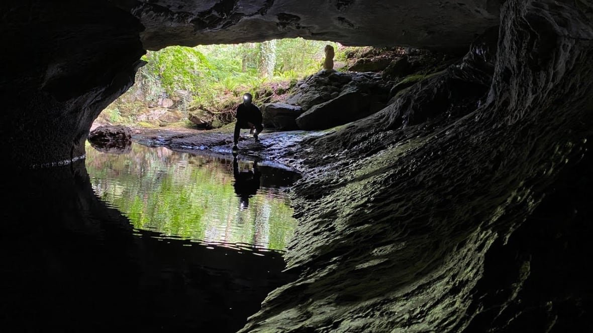 A man with a light on his helmet kneels at the entrance of a water-filled cave.