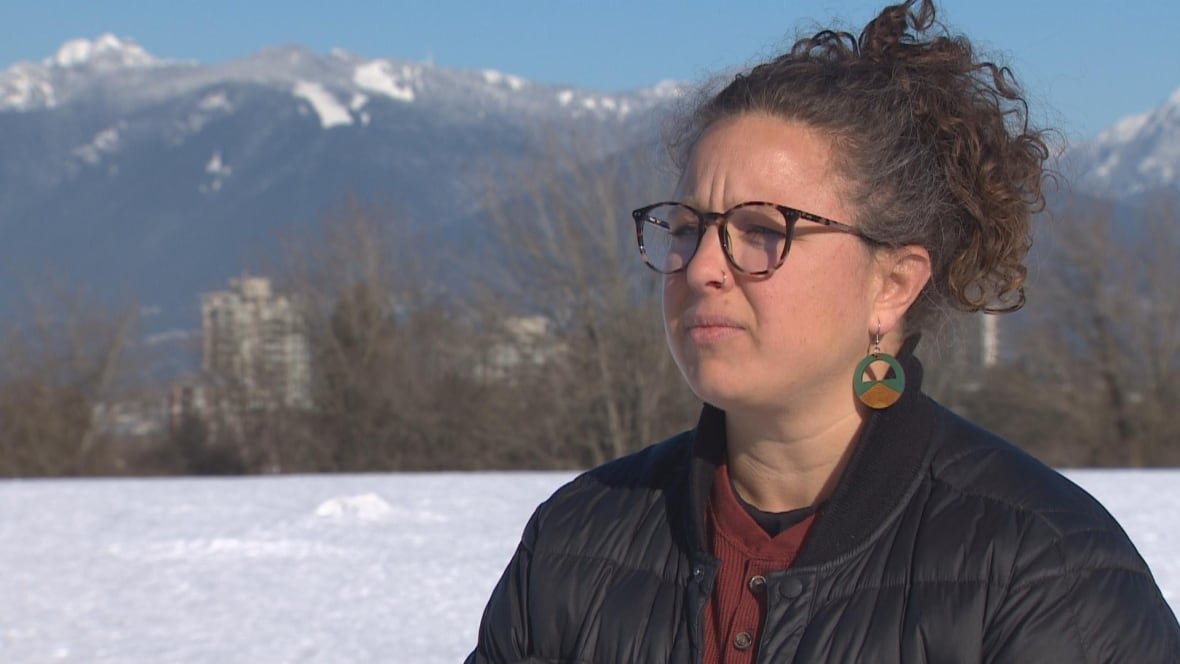 A woman with curly hair is pictured with snow-topped mountains in the background.