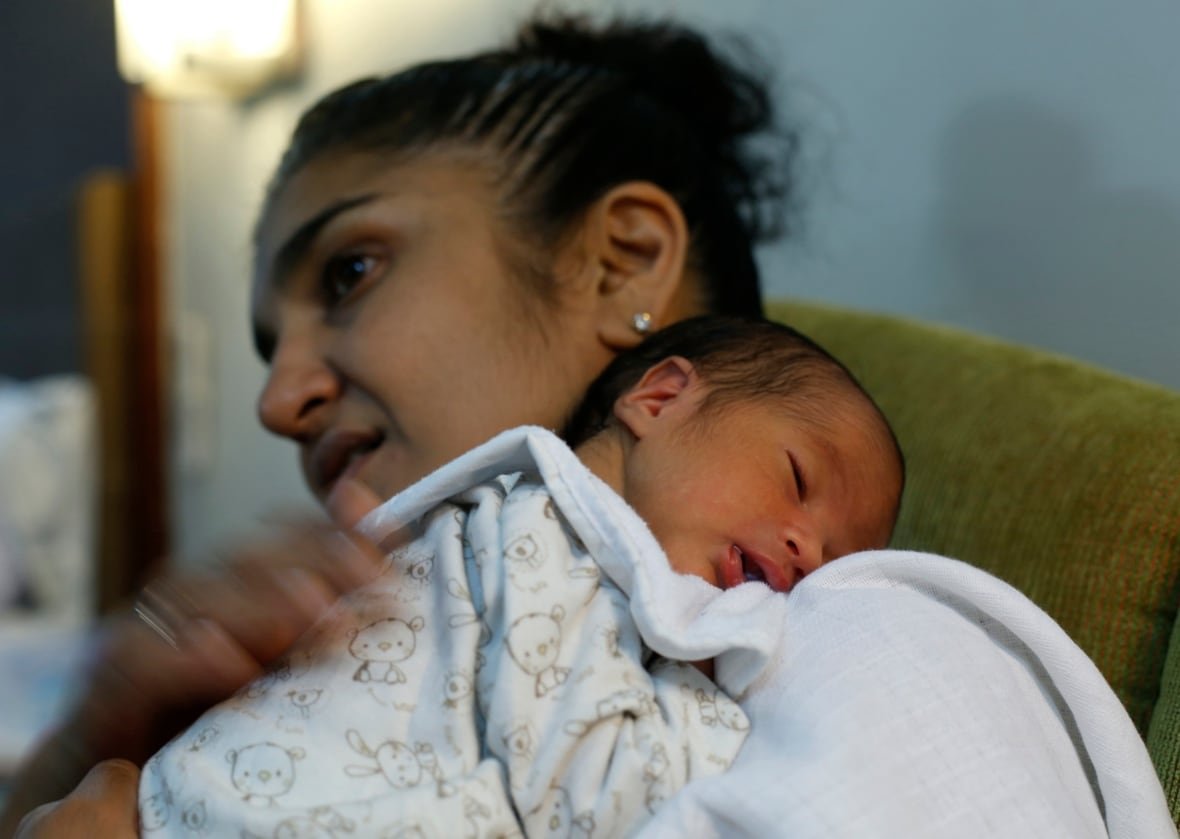 A woman holds a newborn baby on her shoulder. The baby is sleeping. 