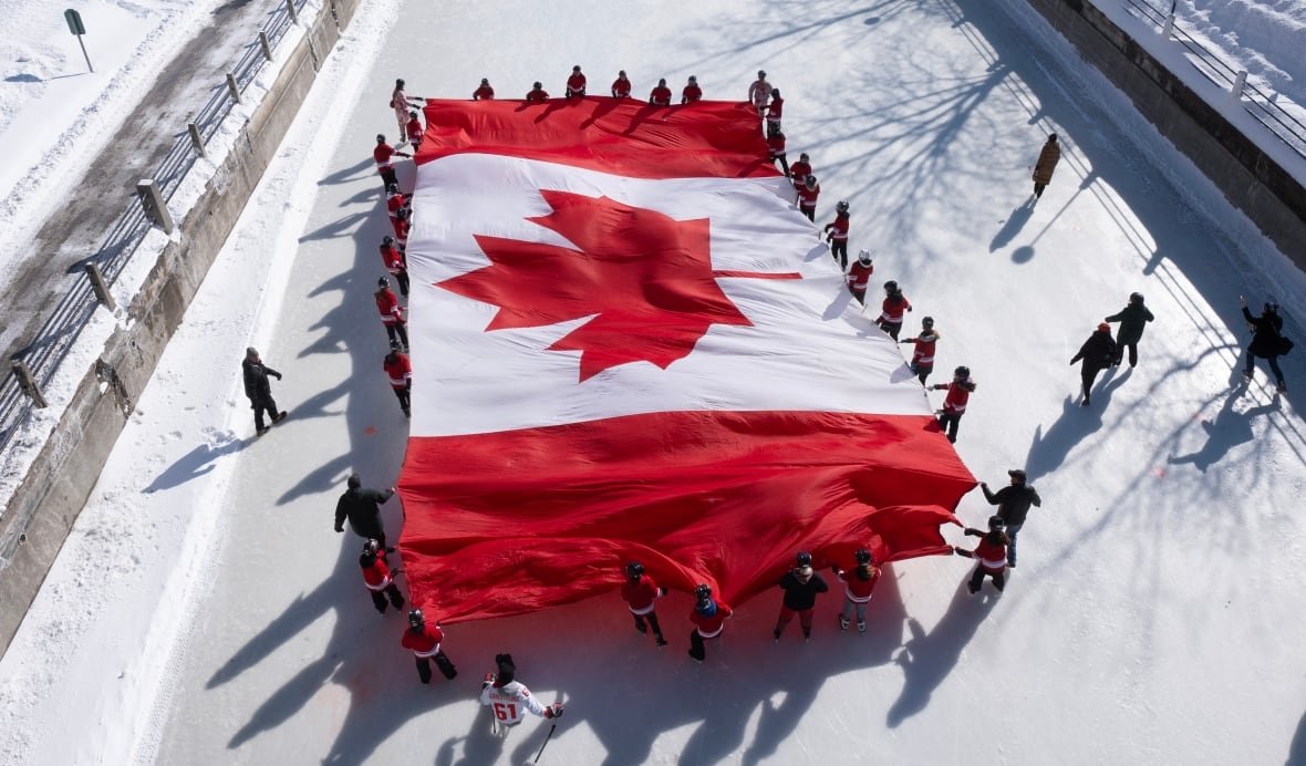 People on ice unfurl a Canadian flag on the Rideau Canal Skateway