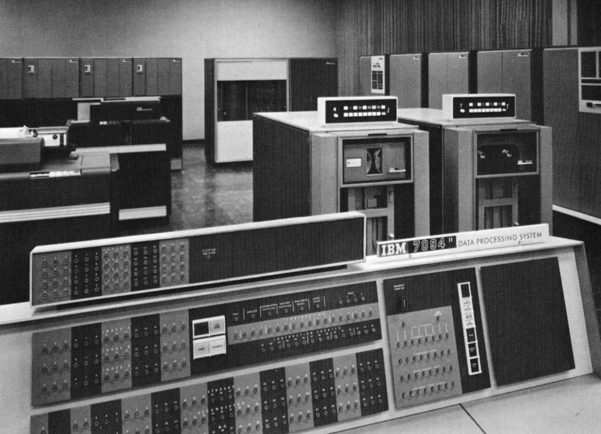 Big, boxy computers with a lot of switches are seen here in a grainy black and white photograph. 