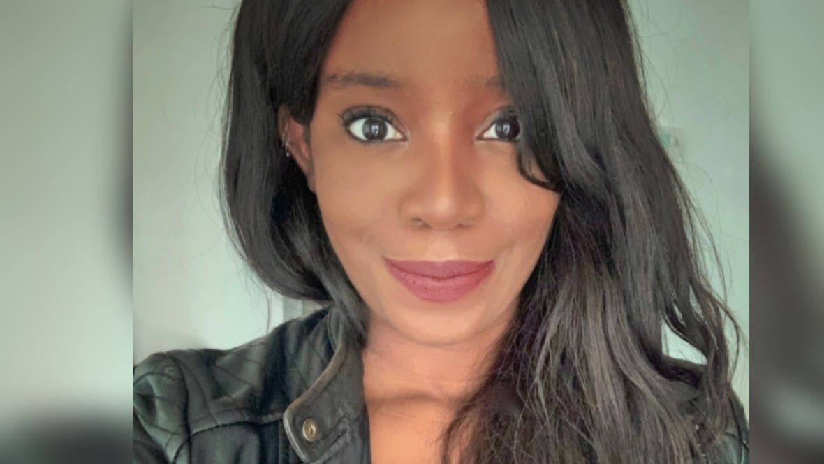A Black woman with long wavy black hair and red lipstick looks at the camera with a closed moith smile.