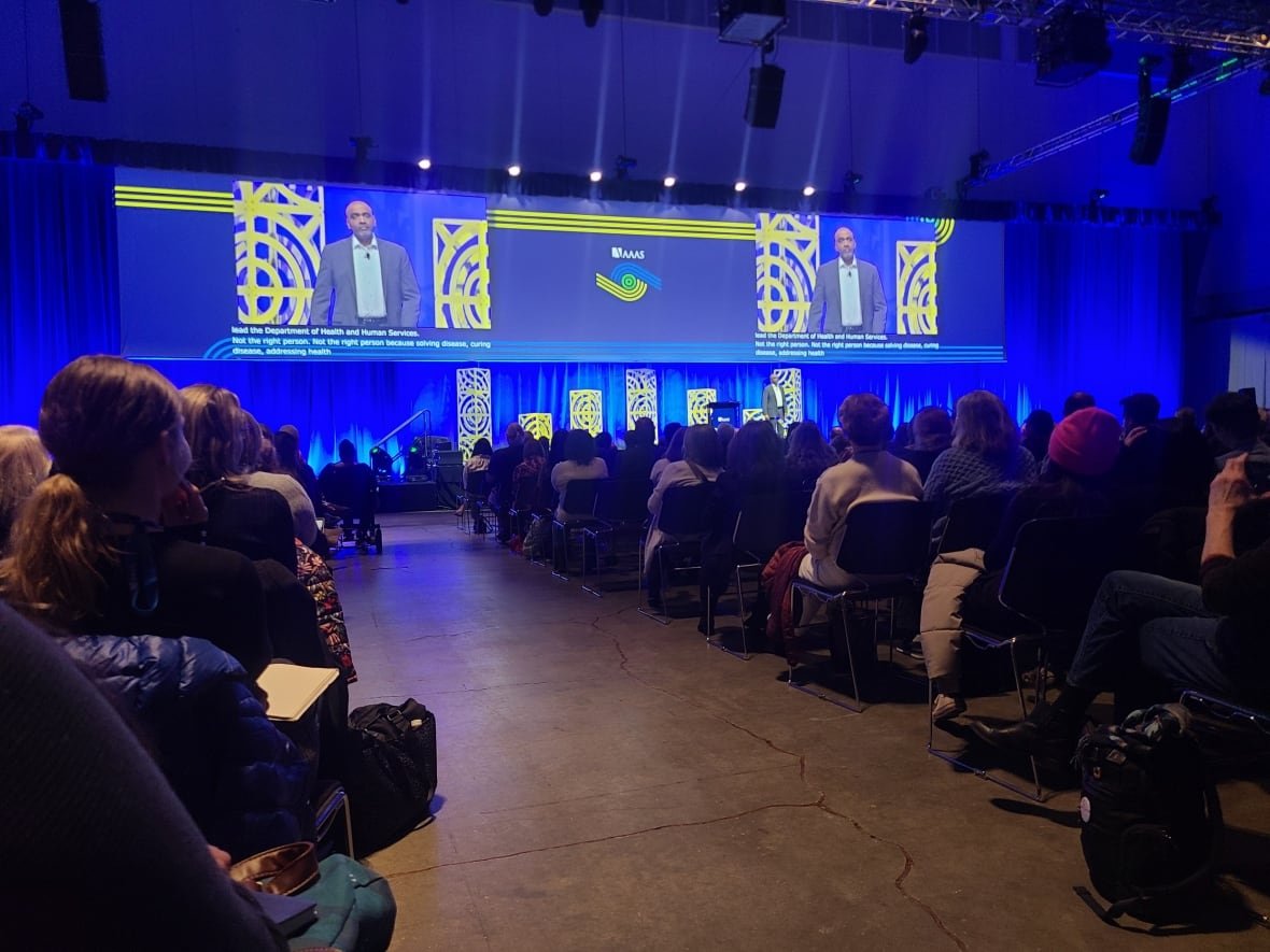 An audience facing a screen with a man on it